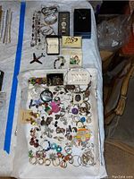 Photo showing a collection of jewelry including necklaces, bracelets, gold-toned watch, and various earrings on a white cloth backdrop.