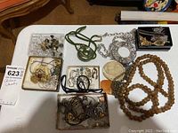 Overview of assorted costume jewelry spread out on table including chains, rings, earrings, and boxed groups of items.