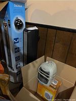 Photo showing Sierra black tower fan in box alongside a white Pelonis space heater and its cardboard packaging.