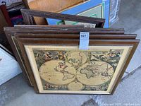 Stack of framed historic map prints with visible wood frames, showing the front detailed map print with Latin titles and artistic border, all framed similarly on board without glass, with additional empty wooden frames behind.