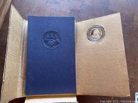 Open blue folio with embossed seal on left and coin insert on right