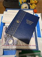 Photo of the Jefferson Nickels coin book with blue cover, gold lettering, and some papers underneath.