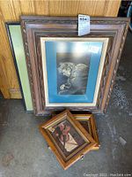 Photo showing the full collection of framed art including one large framed drawing and four small framed prints arranged on the floor leaning against a wall.
