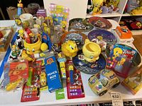 Wide view of lot showing glassware, figurines, plates, PEZ dispensers, toys, and stationery items featuring Tweety Bird and Looney Tunes characters