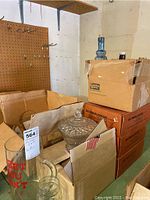 Photo showing boxes and assorted glassware including a decorative bowl with lid, bottles and glass pitcher inside boxes.