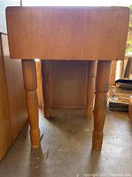 Front view of the vintage maple butcher block showing thickness of the block top and turned legs. Visible surface wear and use marks.