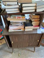 Front view of vintage wooden record cabinet showing stacked books on upper shelves, with closed lower two-door cabinet with brass knobs.