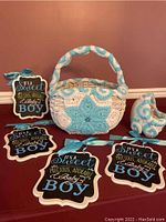 Set of four scalloped wooden signs and two white woven baskets decorated with blue and white crochet work for baby boy announcement shower