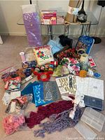 Full overview image of all craft remnants including fabric pieces, ribbons, threads, stickers, stencils, and accessories scattered on the floor and under a glass table.