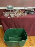 Photo showing Cuisinart electric griddle, mixed glass dishes, and large green plastic bin on burgundy tablecloth