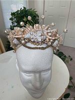 Front view of the handmade seashell crown on a white foam mannequin head showing the seashells, pearl beads, and gold-tone decorative chain.