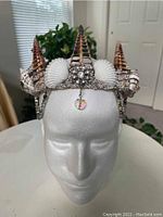 Front view of handmade mermaid crown on white foam head, showing large spiral seashells and rhinestone decorations.