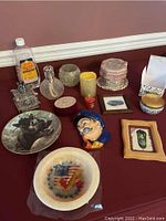 Photo of various home decor items including plates, figurines, candles, framed art, and candle holders arranged on a red table.