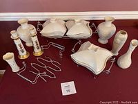 Full lot showing all ceramic items including Lido candlestick holders, vases, tea light warmer, adjustable metal pot trivet, and storage bin on table against red wall