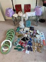 Full lot overview showing purple lampshades, tins, trims, floral rings, lace and ribbons arranged on floor and glass table
