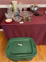 Wide view of lot showing glass vases in varied styles, clear and colored, two flower frog holders, multiple serving dishes, and electric fondue pot with accessories on a burgundy tablecloth.