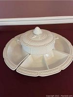 Top view of white ceramic lazy Susan with hobnail pattern, central bowl with lid and artichoke finial, and surrounding divided wedge-shaped trays.