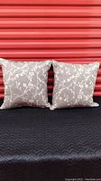 Pair of two gray linen toss cushions with silver embroidery in cherry blossom design shown against a red corrugated metal background.