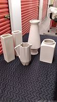 Five white ceramic vases in various shapes and sizes arranged on a pad.