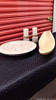 Photo showing round capiz shell bowl, oval capiz shell bowl, two West Elm rustic stone-look candle holders, and two pillar candles on black surface with red background.