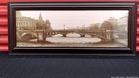 Full view of the framed sepia-toned panoramic photograph of Pont Notre Dame bridge in Paris. The scene includes the bridge and surrounding riverbank buildings with a vintage tone.
