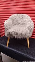 Front view of light gray furry accent chair with light wood legs, showing plush upholstery and armrests.