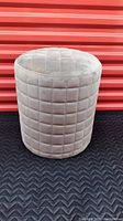 Side view of gray velvet cylinder ottoman showing quilted square pattern and padded seat.
