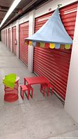Wide view of the Ikea kids play set including wall canopy, table, stools, toy bin, and smock in a storage hallway