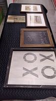 5 pieces of kid's art including distressed frame 'Hugs and Kisses' print, small chalkboard, wolf canvas, and two framed prints laid out on black cloth.