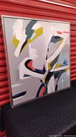 Framed modern abstract artwork, showing the full front view with the painting of abstract shapes and colors on canvas in a metal frame.