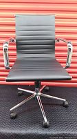 Front view of modern black vinyl office chair with horizontal stitching on back and seat, chrome arms, five caster wheels, and chrome base.