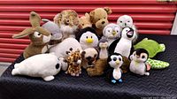 Group photo of 16 stuffed animals including rabbit, penguin, bear, owl, turtle, dolphin, giraffe, seal and others on a black surface
