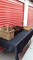 Four wicker items displayed on black cover against red storage background: 2 dark rectangular baskets with handles, 1 large light rectangular tray, and 1 tall light basket with fixed handles.