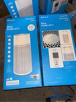 Two Blueair Pure 411+ air purifiers in their original blue boxes, showing product images and some specifications