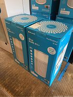 Two boxed Blueair Blue PURE 411+ air purifiers side by side showing brand and model information.