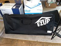 Black fabric carrying case for EZ Up folding chair with EZ Up logo on top