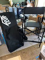 Two black folding director's chairs with black carrying cases placed on floor inside a room with other household items visible in the background.