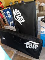 Two black carrying cases for EZ Up folding director chairs standing upright and lying down showing the logo