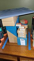 Photo of stacked brown and blue boxes labeled with security sensor types and yard sign stakes, with some instruction booklets visible on top.