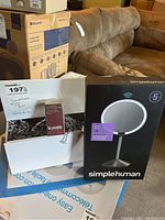 Photo of boxed SimpleHuman mini sensor mirror and La Prairie beauty products box together on a table, also showing part of a couch and other boxes in background.