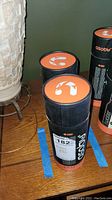 Two cylindrical Asobu Wireless Beat Bottle boxes with black and orange coloring on a wooden surface