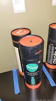 Three black and orange cylindrical boxes upright on a surface showing 'Asobu Wireless Beat Bottle' packaging.