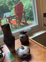 View of three artisan porcelain vases on wooden surface near window, showing different shapes and artful smoky black-brown patterning.