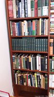 Full bookshelf showing five shelves of various books, predominantly hardcover with some paperbacks, varied colors and sizes.