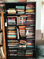 Books on black bookshelf with stacked volumes of classic books, cocktail books, and Dennis the Menace