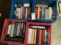 Three plastic milk crate bins containing assorted books, showing a mix of classic literature and music-related titles.