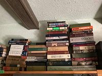Photo showing stacks of classic books including titles by Dickens, C.S. Lewis, and others arranged against a wall below a beam.