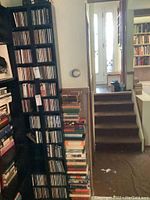 Two black IKEA laminate CD towers shown placed vertically along side a wall, surrounded by stacks of books and other shelving.