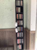 Vertical black shelving unit holding approximately 100 music CDs in jewel cases.