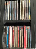 Two shelves with multiple CD jewel cases, showing spines with artist and album titles including classical and jazz music.